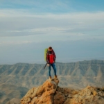 Solo traveler standing on a rocky mountain peak with panoramic views, symbolizing the courage and personal growth gained through adventurous travel.