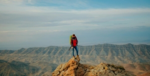 Solo traveler standing on a rocky mountain peak with panoramic views, symbolizing the courage and personal growth gained through adventurous travel.
