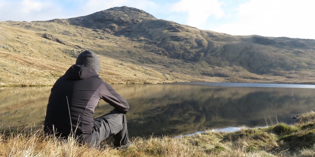 Traveler sitting by a tranquil mountain lake surrounded by scenic hills, capturing a peaceful moment in nature during an authentic travel adventure
