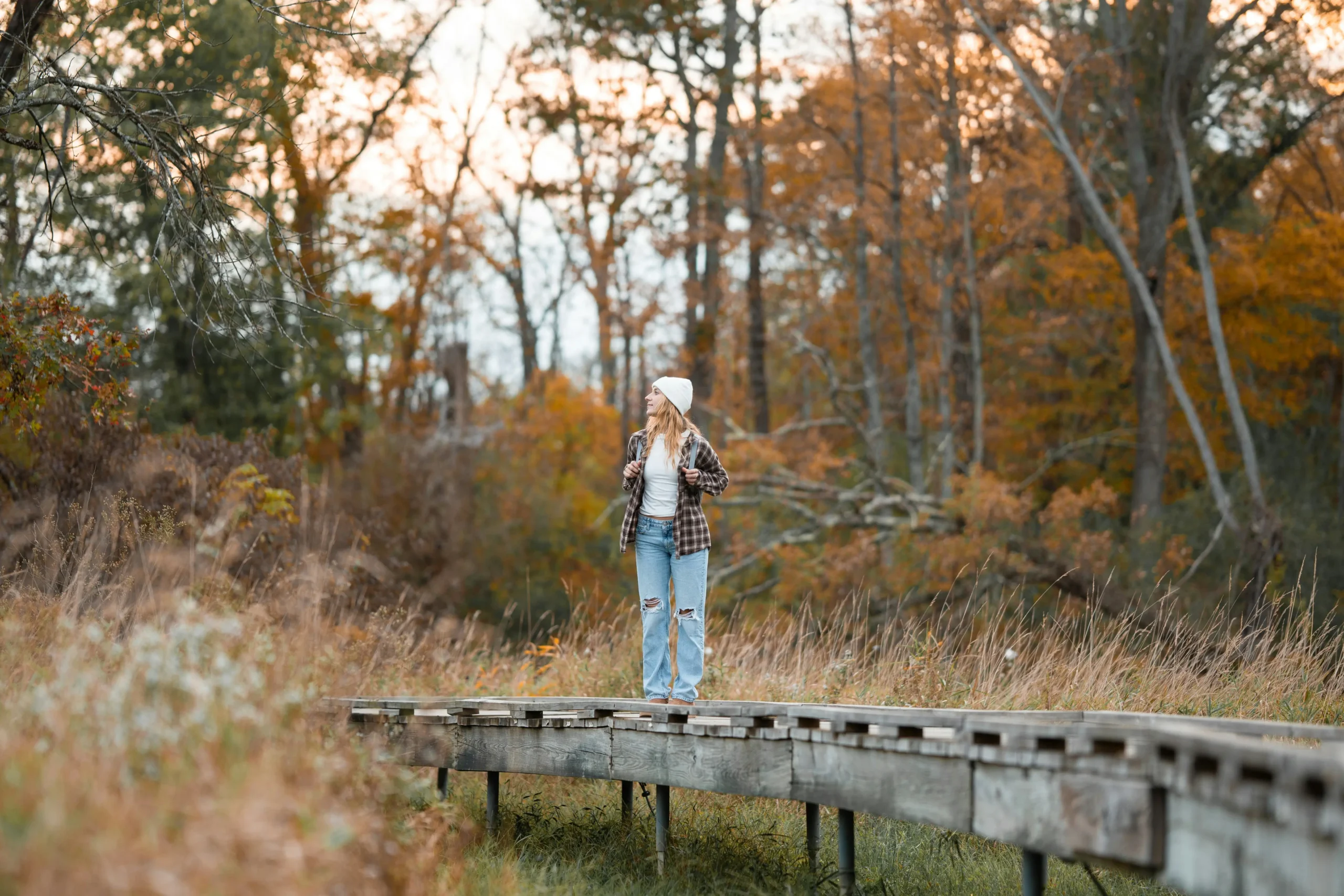 Woman standing on a wooden path in a forest, embracing solitude and reflection during autumn, symbolizing a travel mindset