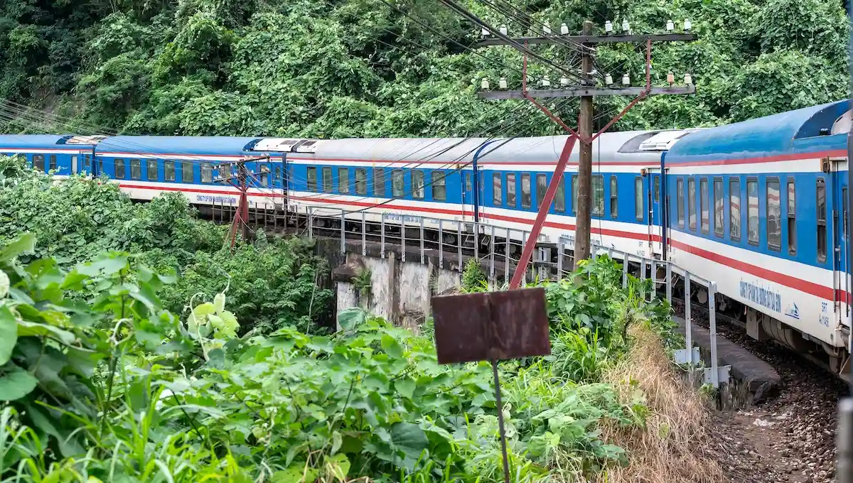 Colorful local train traveling through lush tropical landscape with dense vegetation and local infrastructure, representing authentic transportation experiences over expensive private transfers