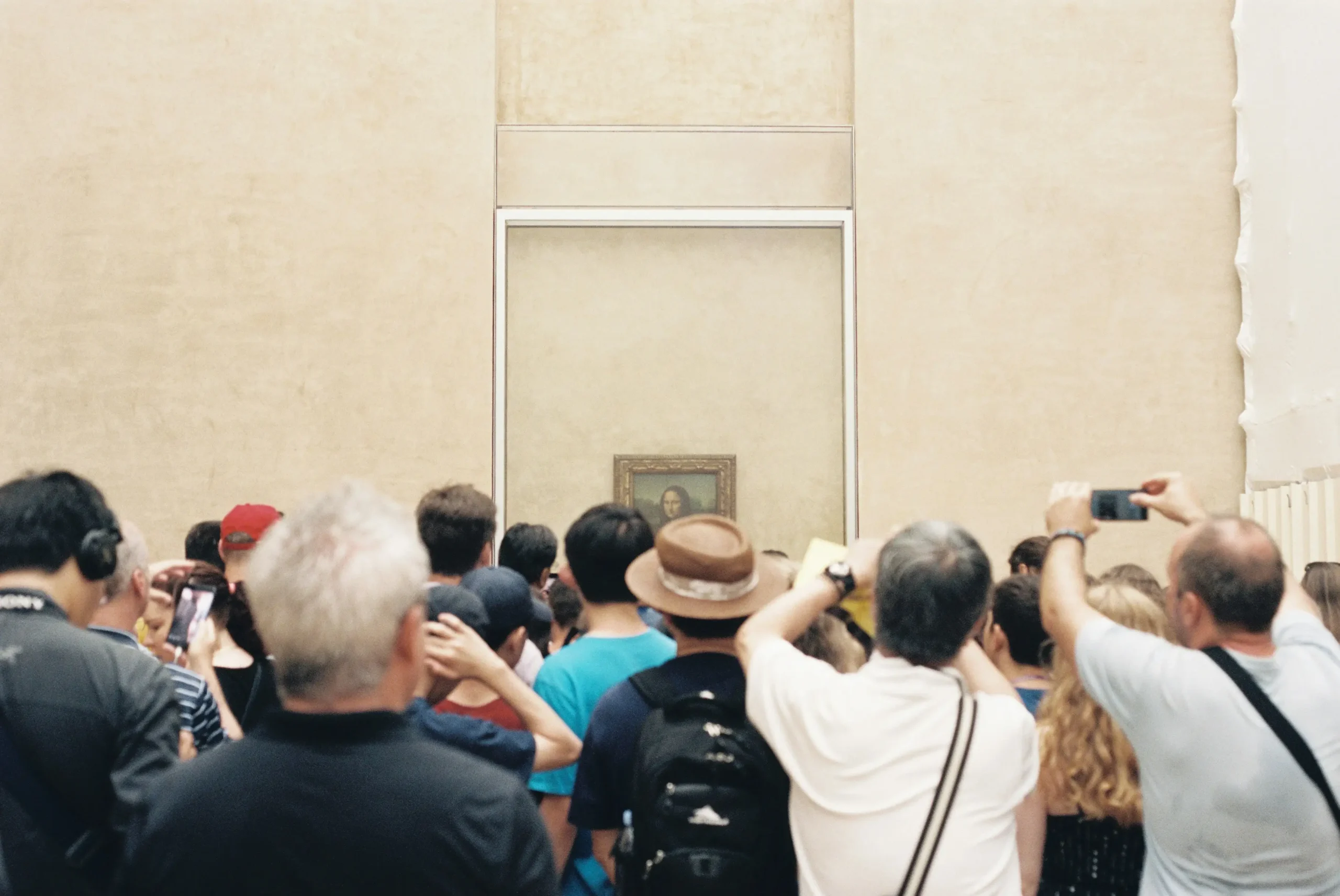 Dense crowd of tourists with phones and cameras all photographing the Mona Lisa in the Louvre museum, showing mass tourism mentality