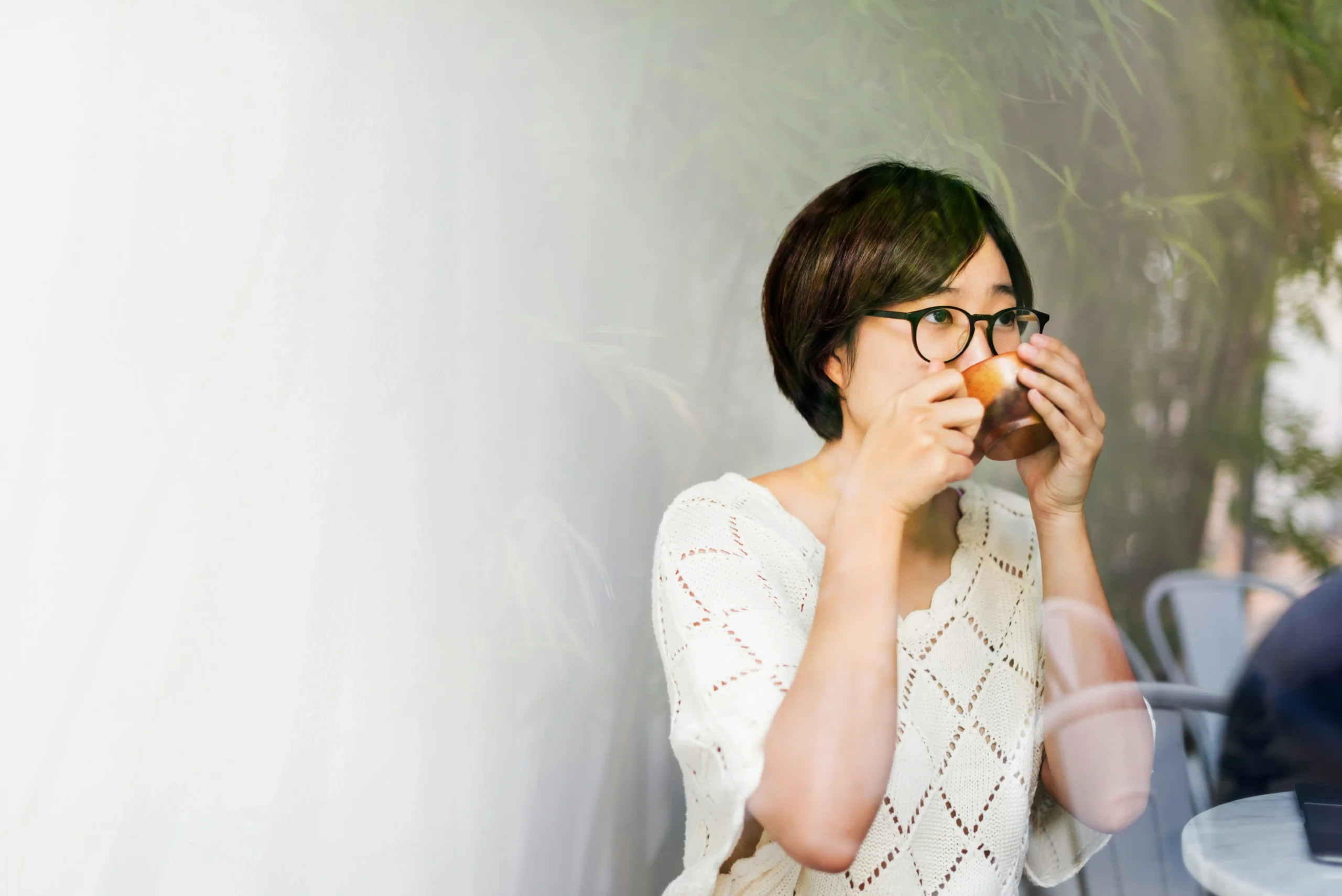 Woman in glasses enjoying coffee thoughtfully at outdoor café, savoring the moment without rushing, representing mindful presence over productivity