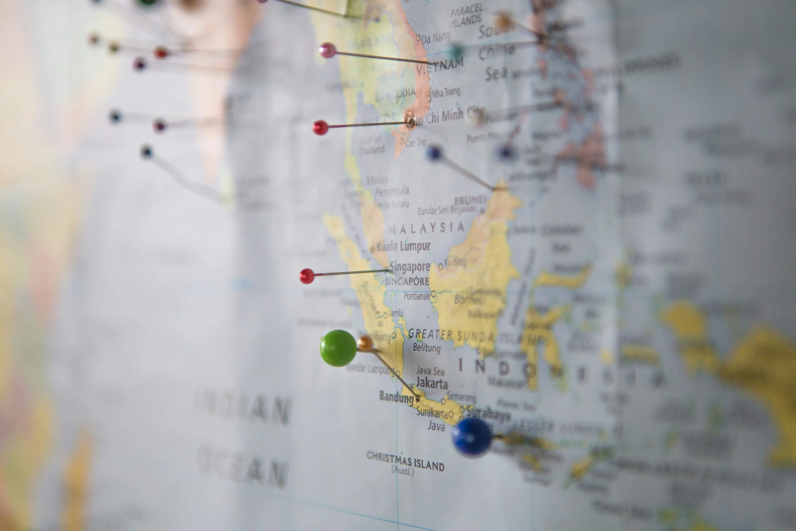 Close-up of world map with colorful pins marking various Southeast Asian destinations including Vietnam, Singapore, and Indonesia with shallow depth of field