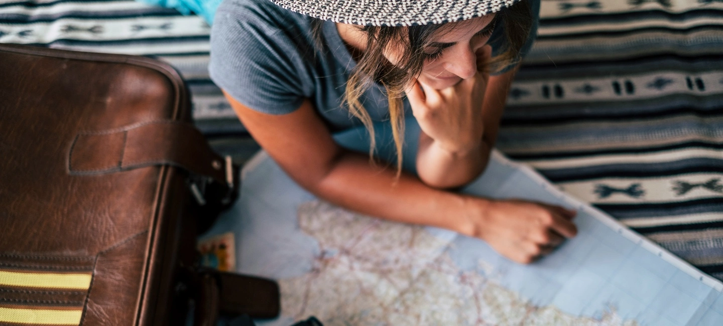 Traveler thoughtfully reviewing a map with suitcase nearby, highlighting effective travel planning and strategic preparation for meaningful journeys.