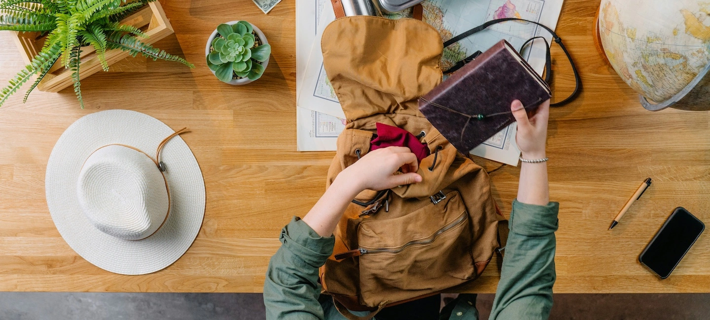 Traveler packing essentials like a journal, hat, and maps thoughtfully laid out, highlighting thoughtful emotional, physical, and cultural preparation for meaningful travel.