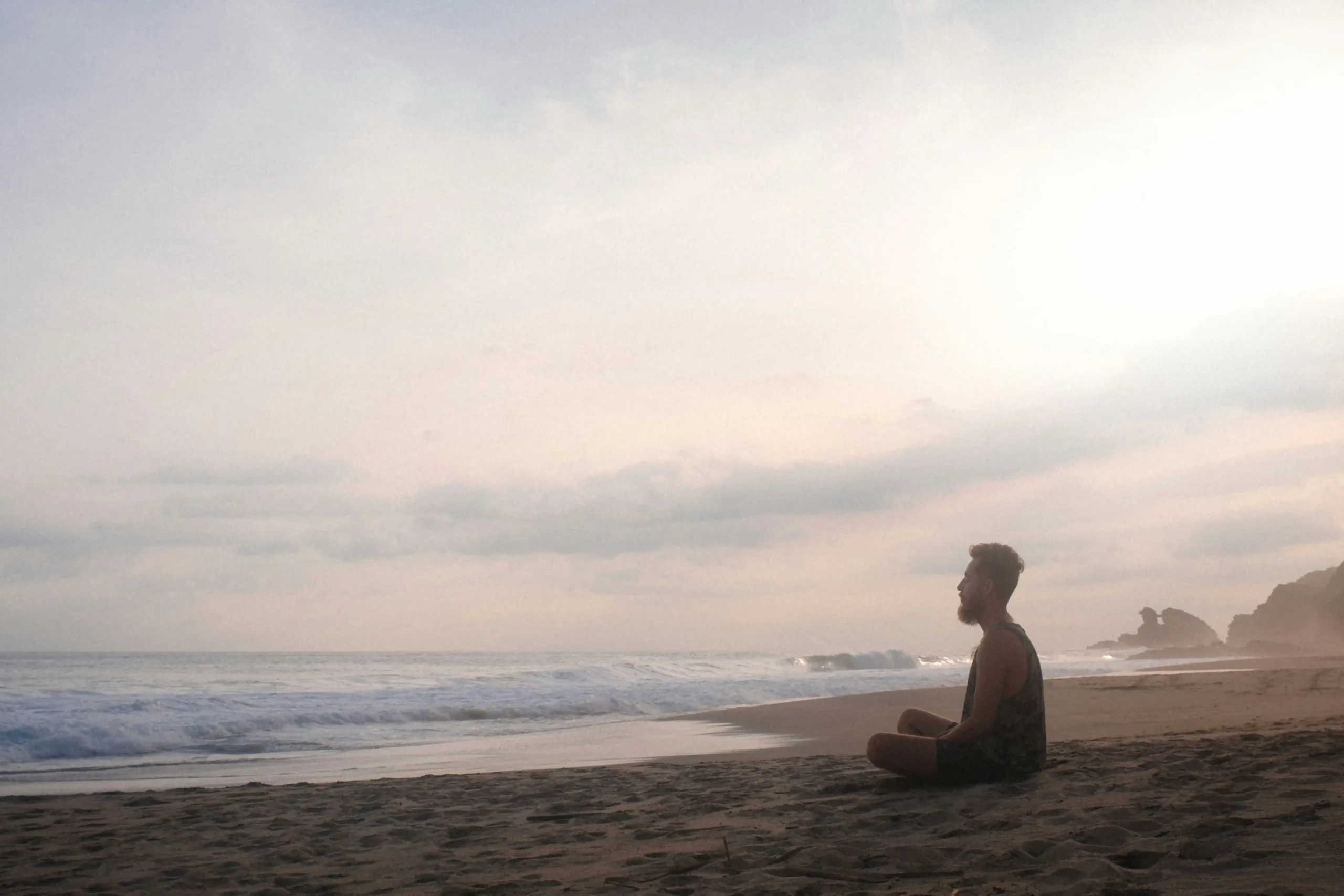  Silhouetted figure sitting in meditation pose on beach at sunset with waves and coastal cliffs, representing inner preparation and mindfulness