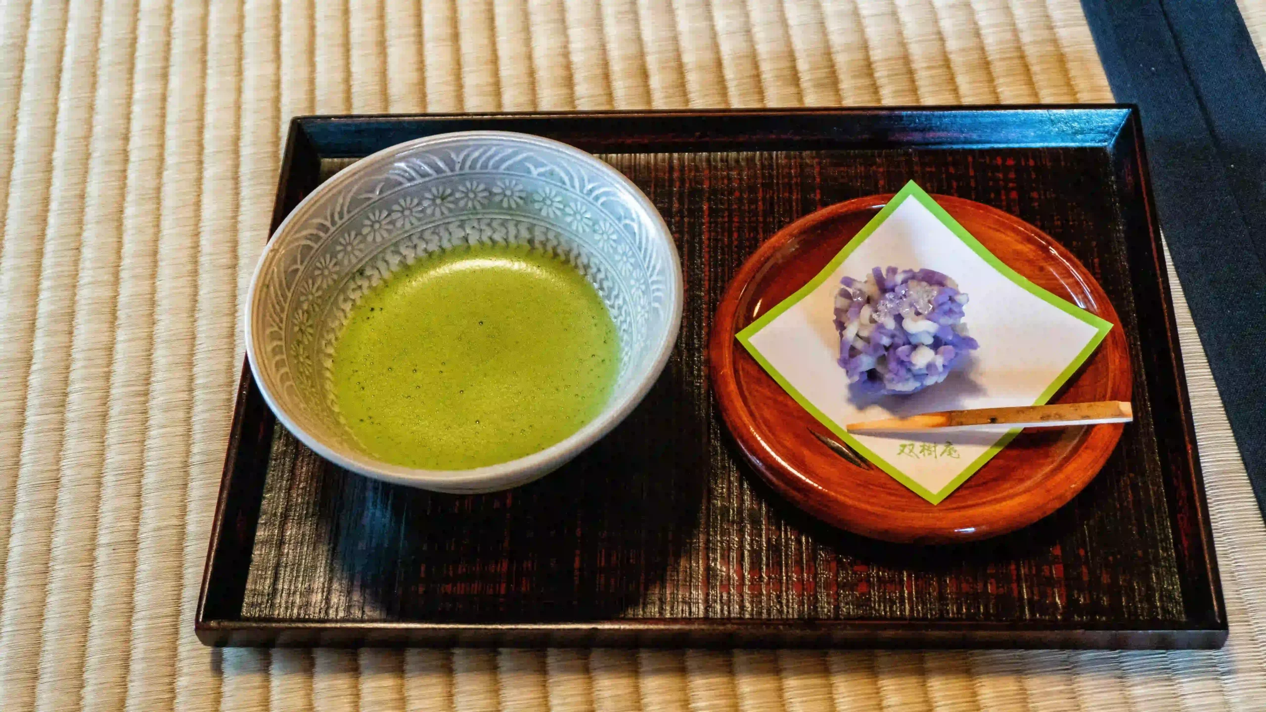  Traditional Japanese tea ceremony presentation with matcha tea in ceramic bowl and seasonal sweet on tatami mat, representing the precise cultural protocols Marcus needed to learn