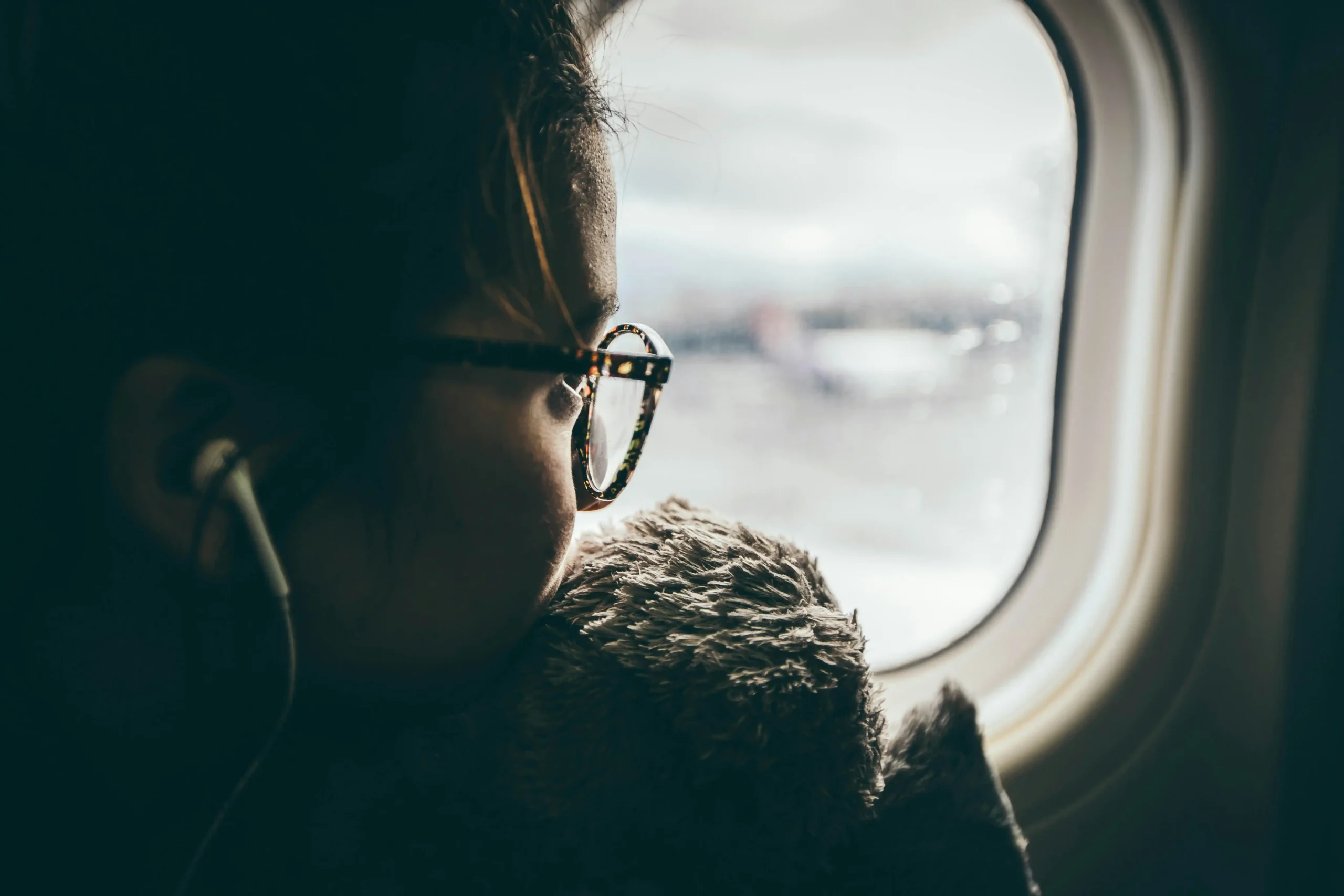  Person with glasses looking pensively out airplane window during flight, representing the contemplative and anxious moments that can arise during travel